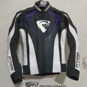 Può includere: Giacca da moto in pelle nera e bianca con dettagli blu. La giacca presenta strisce bianche sulle maniche e sui lati, e il testo "PYTHONS RACING GEAR" è visibile sulle maniche e sul colletto. Un logo è sul petto.