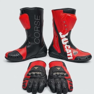 May include: A pair of black and red motorcycle boots featuring the text CORSE and DUCATI, accompanied by a pair of matching black and red motorcycle gloves with the Dainese logo on the wrist straps, designed for protective riding gear.