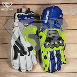 Può includere: Un paio di guanti da moto bianchi, neri, blu e verde neon. I guanti hanno la scritta "SUZUKI" e "GSX". I guanti sono appesi su una superficie di legno. Il marchio "PYTHONS RACING GEAR" è visibile.
