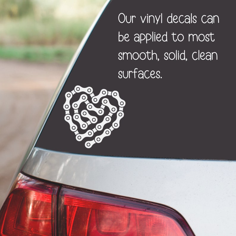 May include: A white vinyl decal of a bicycle chain in the shape of a heart. The decal is on a black background and says "Our vinyl decals can be applied to most smooth, solid, clean surfaces."