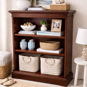 May include: A dark wood bookshelf filled with decorative items. It features a white vase with flowers, framed art, books, a woven basket, and two striped storage bins. Two blue and white vases are on a shelf.