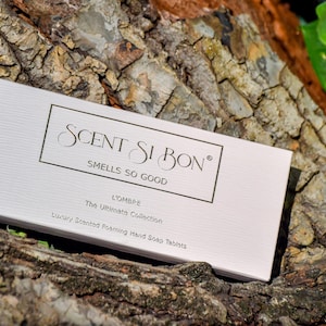 May include: A white box with the text "SCENT SI BON" and "SMELLS SO GOOD" in black lettering. The box also says "L'OMBRE The Ultimate Collection Luxury Scented Foaming Hand Soap Tablets".