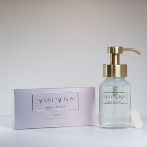 May include: A white box with the text "Scent Swoon" and "Smells So Good" on it. Next to the box is a clear glass bottle with a gold pump dispenser. The bottle is filled with a clear liquid. The bottle has a label that says "Scent Swoon" and "Smells So Good".