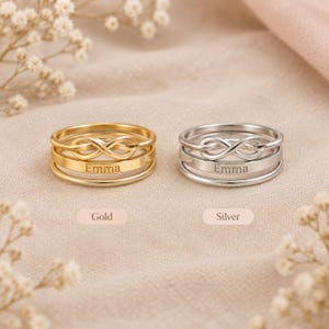 Pode incluir: Dois an&eacute;is empilhados, um em tom dourado e outro em tom prateado, cada um com um s&iacute;mbolo de infinito na banda superior e o nome Emma gravado na banda inferior. Os an&eacute;is s&atilde;o exibidos com as etiquetas Gold e Silver abaixo deles.