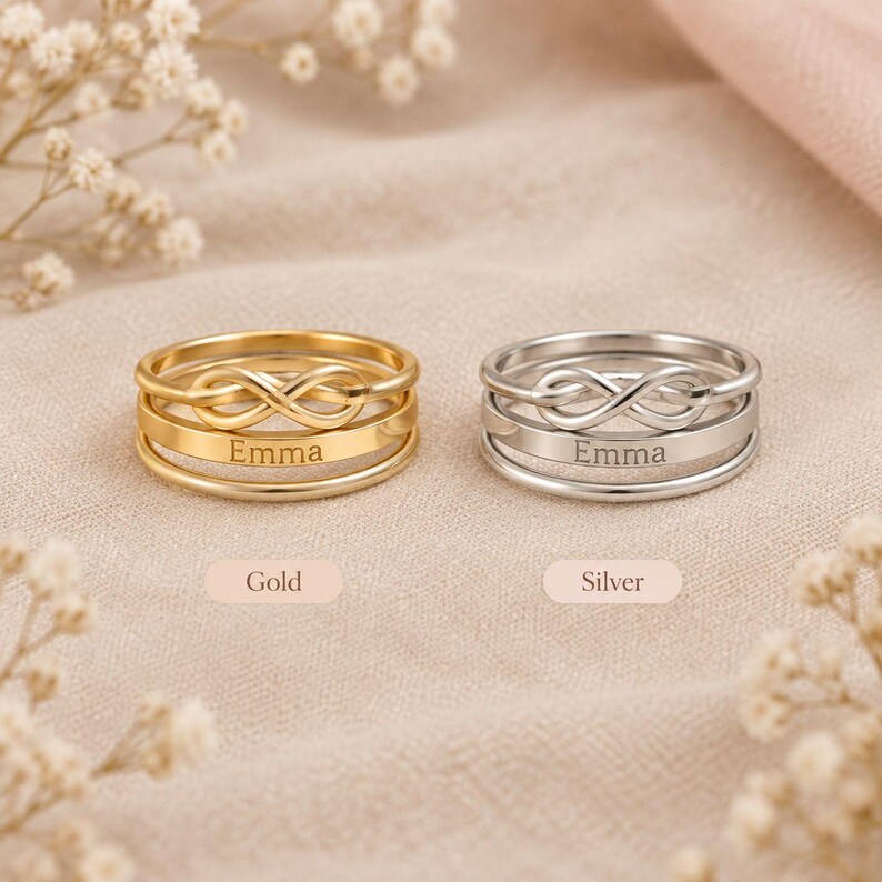 Pode incluir: Dois an&eacute;is empilhados, um em tom dourado e outro em tom prateado, cada um com um s&iacute;mbolo de infinito na banda superior e o nome Emma gravado na banda inferior. Os an&eacute;is s&atilde;o exibidos com as etiquetas Gold e Silver abaixo deles.