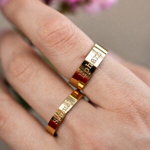 May include: Two polished gold-tone metal bands featuring engraved text. The upper ring displays the name Ephram in a serif font, while the lower ring features the name samuel in a lowercase sans-serif font. Both rings have a flat, smooth surface.