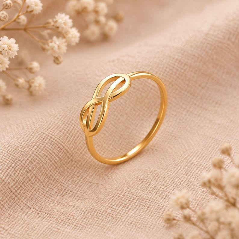 Pode incluir: Um anel de ouro polido com um design central em forma de s&iacute;mbolo do infinito. A banda &eacute; fina e circular, apresentando um acabamento met&aacute;lico liso e reflexivo. O motivo do infinito &eacute; formado por dois la&ccedil;os entrela&ccedil;ados que criam uma forma fluida.