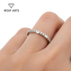 Könnte beinhalten: Ein silberner Ring mit einer durchgehenden Reihe kleiner, klarer Edelsteine. Der Ring befindet sich an einem Finger. Der Markenname "IRGIF ARTS" ist in Schwarz über dem Ring aufgedruckt.