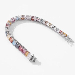 May include: A silver bracelet with a row of colorful gemstones. The gemstones are arranged in a rainbow pattern, with a variety of colors including red, orange, yellow, green, blue, and purple. The bracelet has a clasp closure.