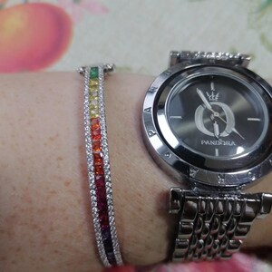 May include: A silver-toned Pandora watch with a dark gray face and a matching bracelet. The bracelet features a rainbow of colorful gemstones. The watch and bracelet are worn on a wrist.