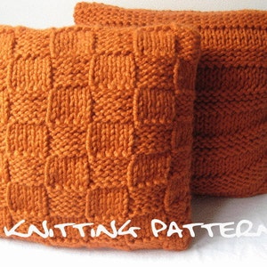 May include: Two orange knitted cushions. One cushion features a textured, checkered pattern, the other a simpler knit design. The cushions are made of thick yarn and are displayed on a white surface. The text "KNITTING PATTERN" is visible.