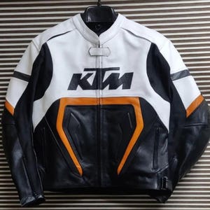 May include: A black and white leather motorcycle jacket with orange accents. The jacket has a zipper closure and the word "KTM" printed on the front.