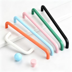 May include: A collection of colorful cabinet hardware, including several long, curved handles in orange, blue, pink, green, and black. Also shown are a white handle, a light blue sphere, and a pink knob. The hardware is designed for furniture.