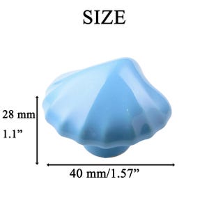 K&ouml;nnte beinhalten: Ein hellblaues Keramik-Muschel-Schrankknauf. Der Knauf misst 28 mm hoch und 40 mm breit. Das Wort "SIZE" ist oben im Bild aufgedruckt.