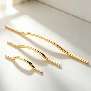 May include: Three gold-colored cabinet pulls in varying sizes. The pulls have a curved, wave-like design. The largest pull is approximately 12 inches long, the medium pull is 8 inches, and the smallest is 4 inches. The pulls are made of metal.