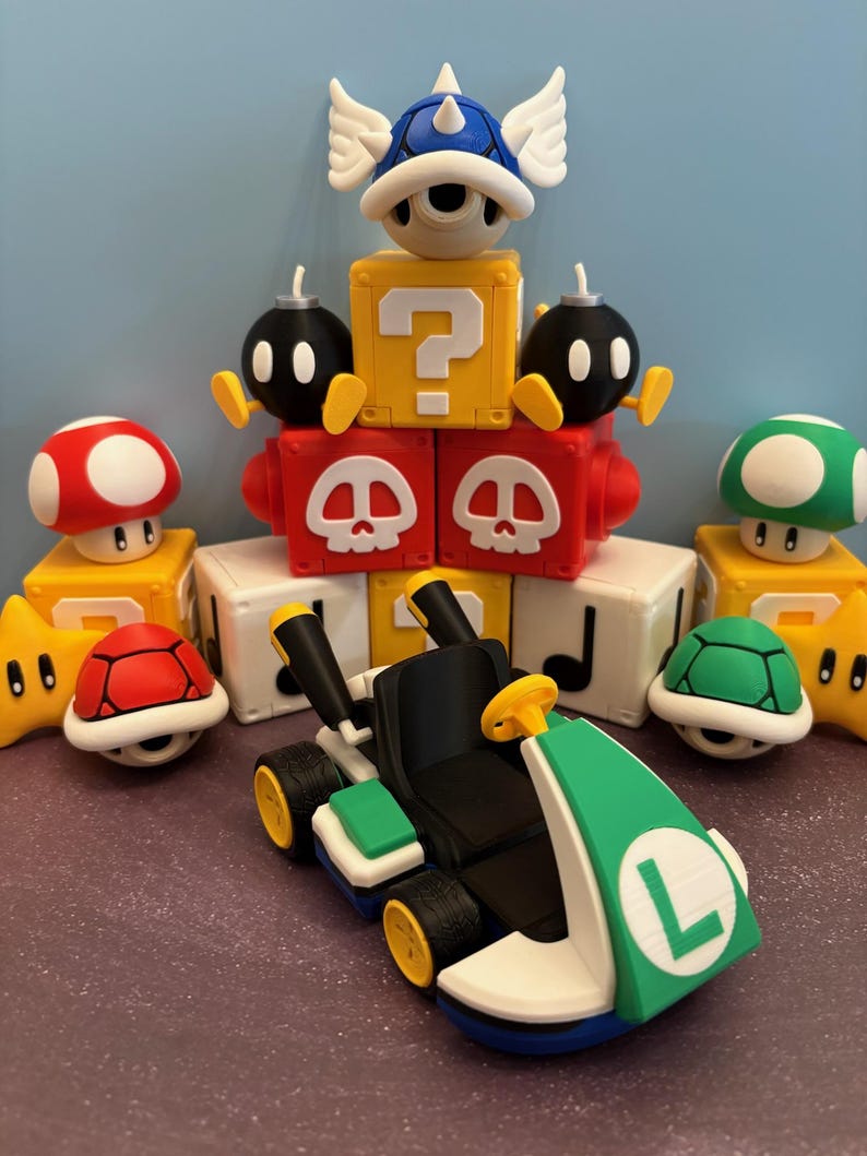 May include: A collection of colorful 3D-printed figures and a kart, inspired by the Super Mario video game series. The kart is black, green, and white, with yellow wheels. Other figures include a red mushroom, a green turtle shell, and a blue shell.