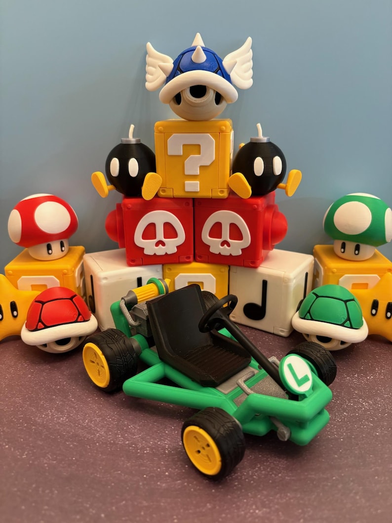 May include: A collection of colorful Mario-themed toys, including a green kart with yellow wheels, a blue shell with wings, red and green mushrooms, and various block figures. The toys are arranged on a purple surface.