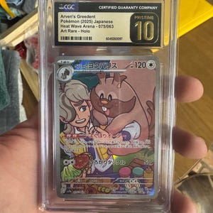 Puede incluir: Una carta de Pokémon calificada con Arven's Greedent del conjunto Heat Wave Arena. La carta es japonesa, etiquetada como Art Rare - Holo, y calificada como Pristine 10 por CGC. El arte de la carta representa un personaje con un Greedent.