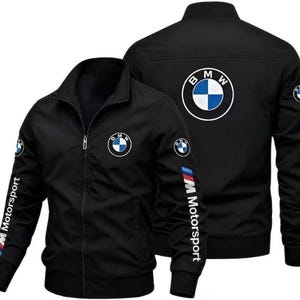 Può includere: Una giacca nera con zip caratterizzata dal logo BMW sul petto e sulla schiena, con la scritta BMW Motorsport e strisce blu, viola e rosse stampate verticalmente sulle maniche. La giacca presenta un colletto rialzato, polsini a coste e chiusura frontale.