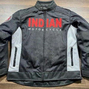 Può includere: Giacca da moto nera con le scritte "INDIAN MOTORCYCLE" in rosso e bianco. La giacca ha un design a rete con pannelli bianchi sui lati e due tasche con cerniera. Una toppa circolare è sulla manica sinistra.