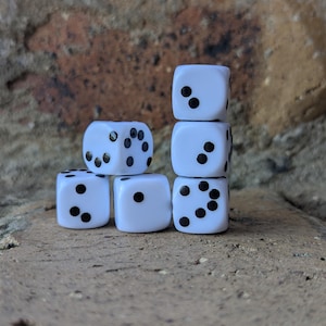 May include: Six white dice with black dots are stacked on a brick surface. The dice are arranged in a pyramid shape, with each die displaying a different number of dots. The dice are a classic gaming accessory.