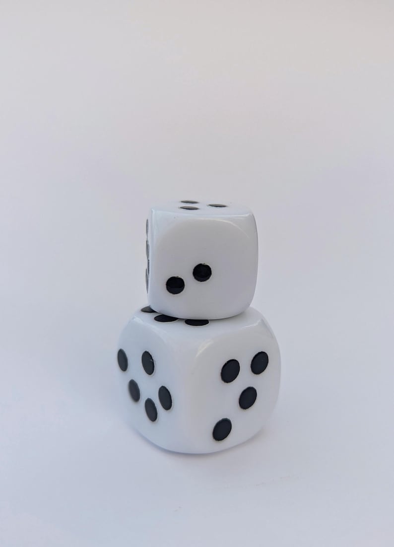 May include: Two white dice stacked on top of each other. Each die has black dots representing numbers. The dice are set against a plain white background.