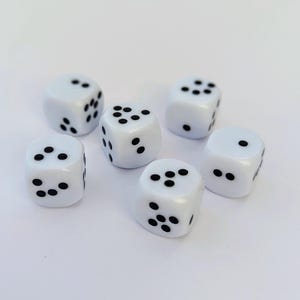 May include: Six white dice with black dots are arranged on a white surface. Each die has a different number of dots, ranging from one to six. The dice are evenly spaced and appear to be new.