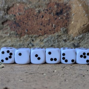 May include: Six white dice with black dots are arranged in a row. The dice are on a rough, brown surface, with a blurred brick wall in the background. Each die shows a different number of dots, from one to six.