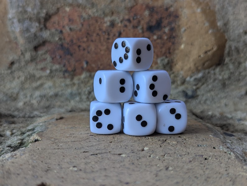May include: A stack of six white dice with black dots. The dice are arranged in a pyramid shape, with three dice at the base, two in the middle, and one at the top. The background is a textured brick wall.
