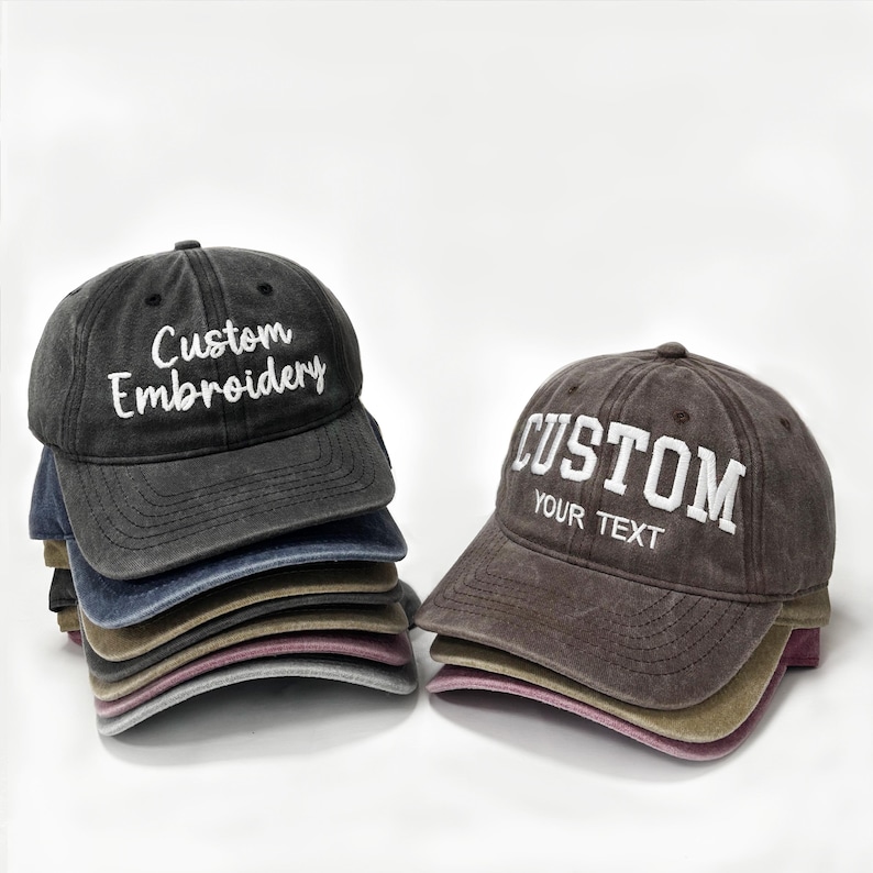 May include: A stack of custom embroidered baseball caps in various colors, including black, blue, and brown. One cap displays "Custom Embroidery" in white, while another says "Custom Your Text". The caps have a vintage, worn look.