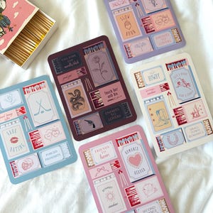May include: Four rectangular sticker sheets featuring various matchbox-themed illustrations and romance tropes. Each sheet displays small boxes, matchsticks, and text labels like "Enemies to Lovers," "Fake Dating," "Howdy," and "Friends to Lovers" in pastel and dark colour palettes.