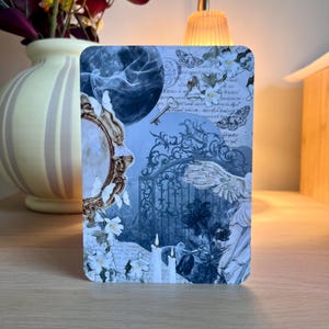 Op de afbeelding: Een rechthoekige print met een collage van afbeeldingen in blauwtinten. Het ontwerp bevat een volle maan, vlinders, een sleutel, een spiegel, een poort en kaarsen. De print heeft een vintage, etherische esthetiek.