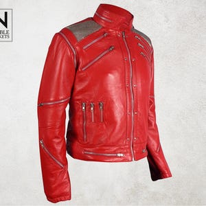Puede incluir: Chaqueta de cuero roja brillante con m&uacute;ltiples cremalleras plateadas y cuello alto. La chaqueta presenta un dise&ntilde;o acolchado en los hombros y el logotipo "Noble Jackets".
