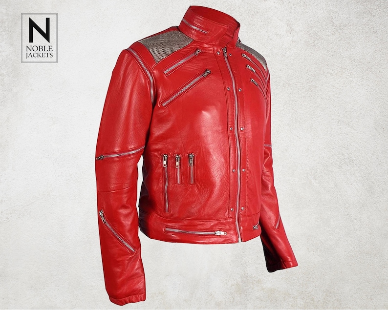 Puede incluir: Chaqueta de cuero roja brillante con m&uacute;ltiples cremalleras plateadas y cuello alto. La chaqueta presenta un dise&ntilde;o acolchado en los hombros y el logotipo "Noble Jackets".