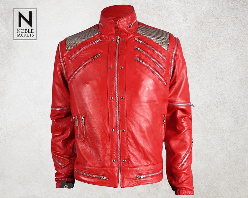 Puede incluir: Chaqueta de cuero roja vibrante con cremalleras y detalles plateados. La chaqueta presenta un cuello alto, m&uacute;ltiples bolsillos con cremallera y adornos plateados en los hombros. El logotipo de Noble Jackets es visible.