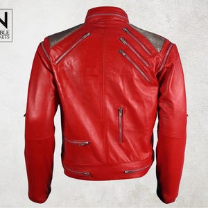 Puede incluir: Chaqueta de cuero rojo brillante con m&uacute;ltiples cremalleras plateadas y cuello alto. Los hombros tienen un panel plateado texturizado. El logotipo "Noble Jackets" est&aacute; en la esquina superior izquierda.
