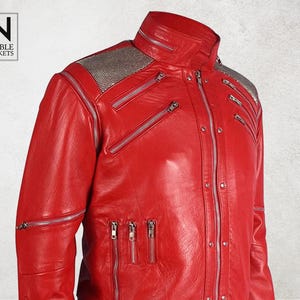 Puede incluir: Chaqueta de cuero roja vibrante con m&uacute;ltiples cremalleras plateadas y cuello alto. La chaqueta presenta un panel plateado texturizado en los hombros. La marca "NOBLE JACKETS" est&aacute; en un recuadro blanco.