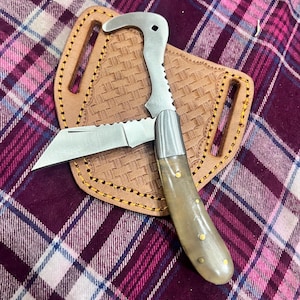 May include: A stainless steel folding knife with a bone handle and a leather sheath. The knife has a serrated blade and a hook on the end of the handle.