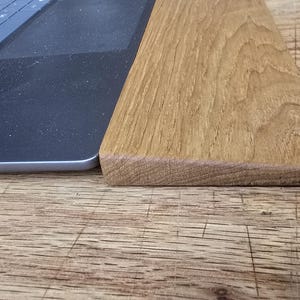 May include: A section of a light brown wooden board next to a laptop. The wood has a natural grain pattern and a smooth, finished edge. The laptop is black with a keyboard visible.