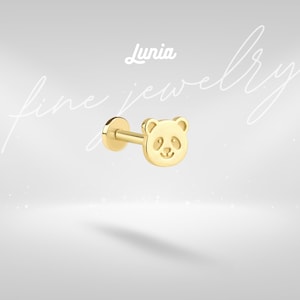 May include: A gold-colored stud earring featuring a panda bear design. The panda's face is detailed with etched eyes, nose, and a smiling mouth. The earring has a flat back and a post for insertion. The word "Lunia" is written above the earring.