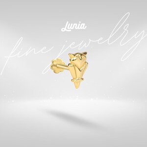 Pode incluir: Um brinco de ouro com design de coruja. O brinco tem um pino com uma parte traseira em forma de flor. A palavra "Lunia" está acima do brinco, e as palavras "fine jewelry" estão escritas em itálico.