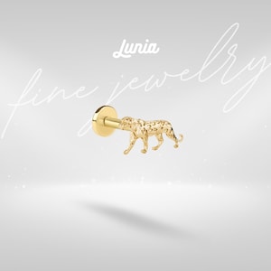 May include: A gold-colored stud earring featuring a detailed leopard design. The earring has a flat, circular backing and a post. The word "Lunia" is written in cursive at the top of the image, with the words "fine jewelry" written in cursive on the left side.