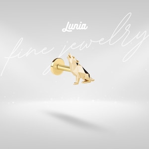 May include: A gold-colored stud earring featuring a geometric wolf design. The wolf is howling, with a detailed, faceted appearance. The earring has a flat back and a post for piercing. The brand name "Lunia" is visible in the upper center.