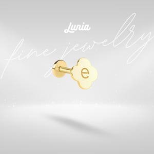 May include: A gold-colored stud earring with a four-leaf clover design and the letter "e" in the center. The earring is part of the "Lunia fine jewelry" collection, as indicated by the text in the image.