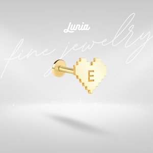 May include: A gold-colored stud earring featuring a pixelated heart design with the letter "E" in the center. The earring has a post and backing. The word "Lunia" is written in cursive at the top of the image. The words "fine jewelry" are written in cursive in the background.