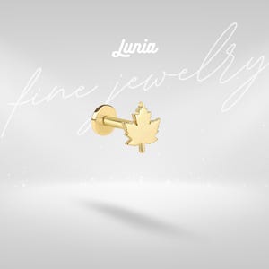 Könnte beinhalten: Ein goldfarbener Ohrring mit flacher Rückseite und Ahornblatt-Design. Der Ohrring hat einen Stecker und eine flache Scheibenrückseite. Das Wort "Lunia" ist kursiv über dem Ohrring geschrieben. Die Worte "fine jewelry" sind kursiv im Hintergrund geschrieben.
