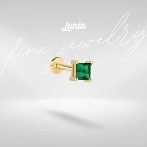 Könnte beinhalten: Ein goldfarbener Ohrstecker mit flacher Rückseite und einem quadratisch geschliffenen, smaragdgrünen Edelstein, der von vier Krappen gehalten wird. Der Text Lunia fine jewelry ist im Hintergrund zu sehen. Der Stecker hat eine flache, runde Basis.