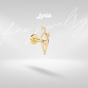 May include: A gold-colored flat back stud earring featuring a cat-shaped charm with an arched tail. The jewelry piece is displayed against a light background with the text Lunia fine jewelry visible in white script and block lettering above the stud.