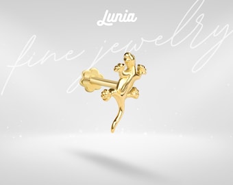 May include: A gold-colored stud earring featuring a lizard-shaped design with a flat, flower-shaped backing. The text 'Lunia fine jewelry' is visible in the background. The earring has a polished, metallic finish and a post for insertion.