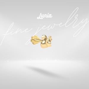 May include: A gold stud earring featuring a squirrel-shaped design with a flat flower-shaped backing. The text Lunia fine jewelry is displayed in white script above the earring. The piece has a polished metallic finish and a post-style closure.